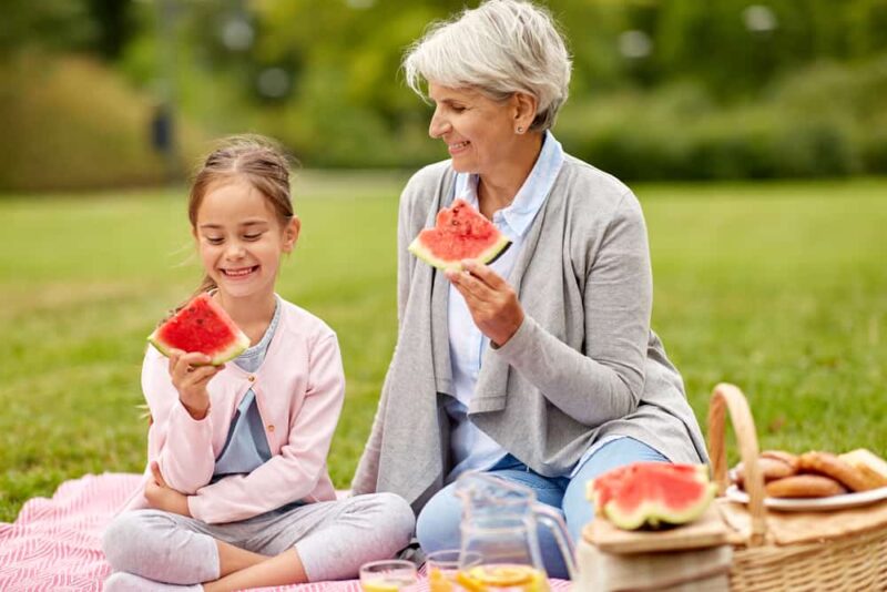 an older woman and young girl picnic together on a nice day, symbolizing how worry and happiness can affect your finances